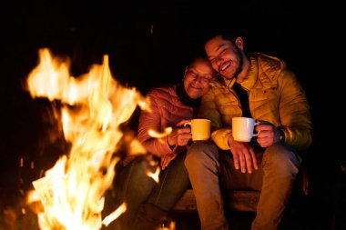 İki kişi kamp ateşinin yanında sıcak bir gece geçirir, ormanda sıcak içecekler yudumlarlar. Sıcak bir şekilde giyinip, ateşin nazik parıltısıyla çevrelenmiş bir şekilde sıcaklık ve mutluluk yayarlar..