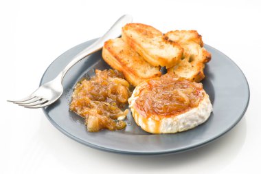 Lezzetli keçi peynirli rulo üzerine tatlı karamelli soğan, ince ve koyu bir tabakta gümüş çatalla kızartılmış ekmek dilimleri ile servis edilir.