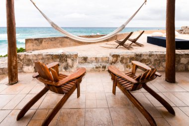 Cozumel Adası 'nda sakin bir sahil sahnesi. Palmiye ağaçları arasında uzanan beyaz bir hamak ve Karayip Denizi' ne bakan tahta şezlonglar..