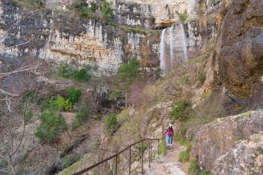Genç bir Asyalı kadın, Albacete, Nacimiento Rio Mundo 'da çarpıcı bir şelalenin yanında yürüyüş yapıyor..