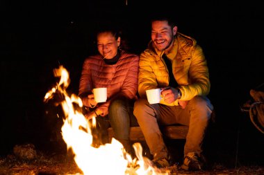 Bir adam ve bir kadın, yıldızlı bir gökyüzünün altında kamp ateşinin keyfini çıkarıyorlar. Ormandaki beyaz bardaklardan sıcak içecekler yudumluyorlar. Turuncu alevler huzur dolu gecede sıcaklık ve ışık verir..