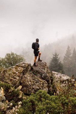 Desierto de los Leones, Meksika 'da sisli ve sık ormanlarla çevrili kayalık bir tepede duran tanınmamış bir erkek yürüyüşçünün arka görüntüsü.