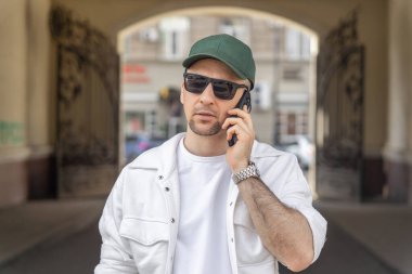 Bir şehir manzarasında yürürken, şık beyaz giysiler içinde cep telefonuyla sohbet eden bir erkek işadamı, iş ve günlük tarzın bir karışımını sergiliyor..