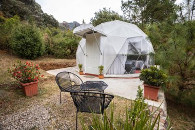 Yeşilliğin ortasına yerleştirilmiş bir cazibe büyüleyici bir geri çekilme sunuyor. Siyah teras sandalyeleri ve canlı saksı bitkileri dışarıyı süsleyerek huzurlu bir ortam yaratıyor..