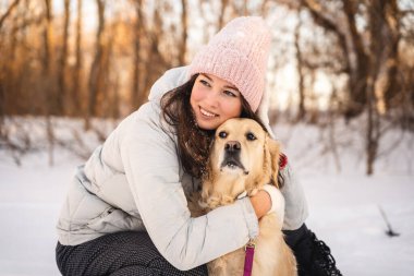 Samimi giyimli genç bir kadın karlı bir ormanda av köpeğini kucaklıyor. Aralarındaki sıcaklık soğukla çelişiyor, neşe ve arkadaşlık sahnesi yaratıyor..