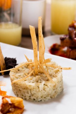 Meksika usulü, gevrek tortilla şeritleriyle süslenmiş, salsa ve yeniden kızartılmış fasulye de dahil olmak üzere çeşitli Meksika mutfağı elementleriyle servis edilen ve yanında bardaklarda taze meyve suyu bulunan bir pirinç tabağı..