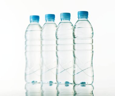 Mavi kapaklı dört şeffaf plastik su şişesi düz bir çizgide duruyor ve alttaki parlak yüzeye yumuşak yansımalar yapıyor. Arka plan temiz, minimalist bir beyaz.