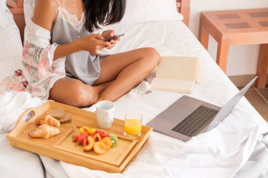 Gece elbiseli tanınmayan bir kadın cep telefonuyla mesajlaşırken dizüstü bilgisayarın yanında oturup kitap okuyor ve sabahları kahvaltı yapıyor.