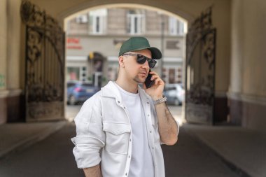 Sıradan beyaz kıyafetli bir erkek işadamı, şehir merkezinde kemer altında dururken akıllı bir telefonla konuşuyor..