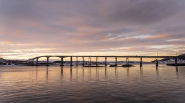 Sakin bir günbatımı, Norveç 'in Senja kentindeki eğimli bir köprü ve sakin sulara sıcak renkler salıyor ve kutup manzarasının dingin güzelliğini gözler önüne seriyor..