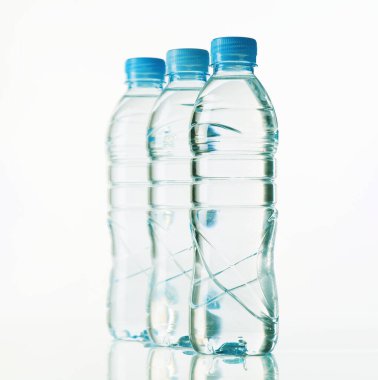 Üç temiz plastik su şişesi beyaz arka planda düzgün bir sırada dizilir. Şişeler mavi kaplamalı, ferahlatıcı bir görünüm sergiliyorlar.