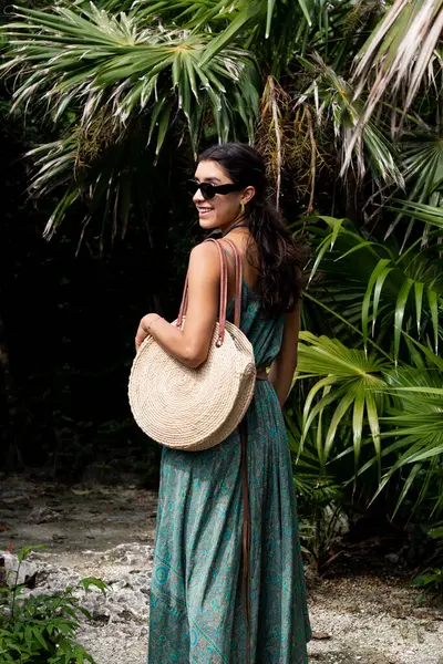 Dalgalı yeşil bir elbise ve güneş gözlüğü takan genç bir kadın, büyük yuvarlak bir torba ile Meksika 'nın Cozumel adasında çevresinin keyfini çıkarırken görülüyor. Bu gizli çekim gösterileri verimli bir tropikal arkaplan.