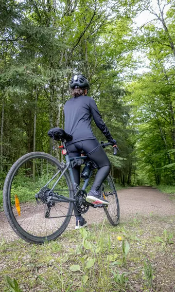 Siyah kıyafetli ve kasklı bisikletçi baharda ormanda bisiklet sürüyor. Bereketli yeşilliklerle çevrili sahne, sakin bir doğal ortamda açık hava macerasını yakalıyor..