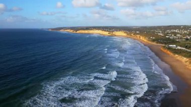 Avustralya 'daki Büyük Okyanus Yolu boyunca uzanan engebeli kıyı şeridinin çarpıcı hava manzarası dramatik uçurumlar, el değmemiş plajlar ve parçalı bulutlu bir gökyüzünün altındaki engin mavi okyanus.