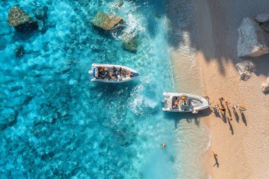 Hava manzaralı tekneler, kumlu sahil ve gün batımında dalgalı mavi deniz. İtalya, Sardinya 'da yaz mevsimi. Motorlu teknelerin, kıyıların, şeffaf sulardaki taşların en iyi insansız hava aracı görüntüsü. Renkli tropikal manzara. Seyahat