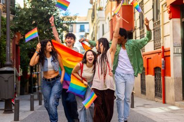 Gurur yürüyüşünde birlikte yürüyen mutlu bir grup genç, gökkuşağı bayrakları sallıyor ve lgbtq artı hakları kutluyorlar.