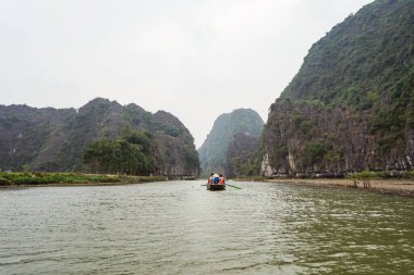 Tanınmayan turistler Tam Coc 'u nehir boyunca kayıkla geziyorlar ve Karst dağlarının güzel manzarasını görüyorlar.