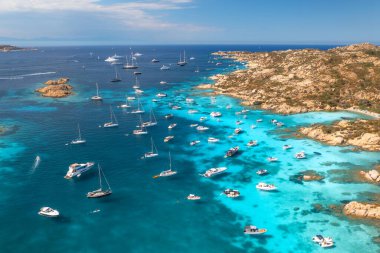 İtalya 'nın Sardunya kentindeki güzel bir sahil koyunun kristal berrak turkuaz sularına demirlenmiş lüks yat ve teknelerin havadan görünüşü yaz tatili ve tatil manzarası yaratıyor. Üst görünüm