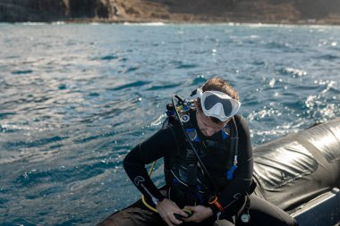 Profesyonel dalgıç dalış ekipmanlarını kontrol ederken şişme teknede oturup denizde dalış keşfine hazırlanıyor.