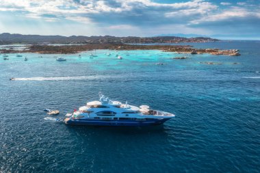 İtalya 'nın başkenti Sardunya' da güneşli bir günün tadını çıkaran demirlemiş teknelerle turkuaz bir Akdeniz kıyısında yüzen büyük, modern yatın havadan görünüşü. Teknelerin en üst drone görünümü