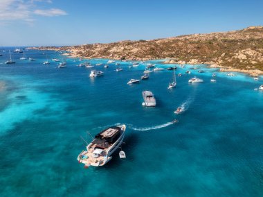 İtalya 'nın Sardunya kentindeki güzel bir sahil koyunun kristal berrak turkuaz sularına demirlenmiş lüks yat ve teknelerin havadan görünüşü yaz tatili ve tatil manzarası yaratıyor. Üst görünüm