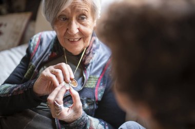 Torununa altın bir madalyon gösteren yaşlı bir kadın, evinde iç açıcı bir anda anılarını ve aile geçmişini paylaşıyor.