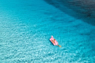 Yazın güneşli bir günde, berrak mavi suyun üzerinde insanların olduğu, şişme pembe flamingo manzarası. Aile fertlerinin teknedeki rahatlama manzarası, İtalya 'nın Sardinya Adası' ndaki masmavi deniz. Seyahat ve tatil