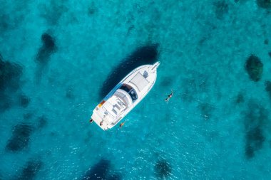 Beyaz bir yatın havadan görünüşü kristal berraklığında turkuaz bir denizde yüzüyor, turistler yakında mutlu bir şekilde yüzüyor ve tropik bir cennette güneşli bir yaz gününün tadını çıkarıyorlar. Okyanusun en üst manzarası