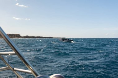 Dalgıçlar, arka planda kayalık bir kıyı şeridi bulunan bir dalış gezisi için motorlu bir tekneyle denize açılıyorlar.