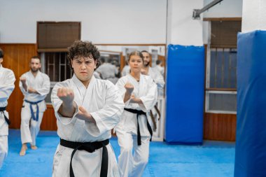 Bir grup Karateka dövüş pozisyonlarını bir dojo 'da uyguluyor, disiplin ve odaklanmayı gösteriyor.