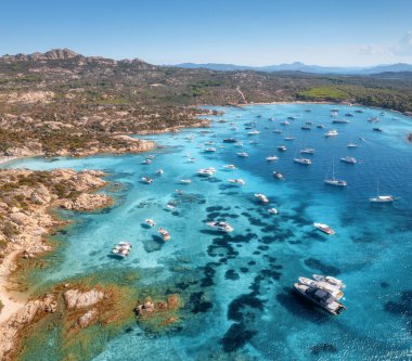 İtalya 'nın Sardunya kentindeki güzel bir sahil koyunun kristal berrak turkuaz sularına demirlenmiş lüks yat ve teknelerin havadan görünüşü yaz tatili ve tatil manzarası yaratıyor. Üst görünüm