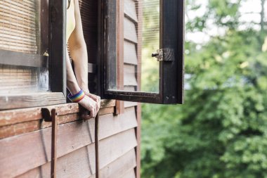 Bir insan, güneşli bir günde, serin bir meltem ve yemyeşil havanın tadını çıkararak, ahşap bir pencerede dinlenir..
