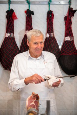 Kıdemli kasap bıçağını biliyor ve kasapta Serrano jambonu dilimliyor. Arka planda da sallanan jambonlar var.
