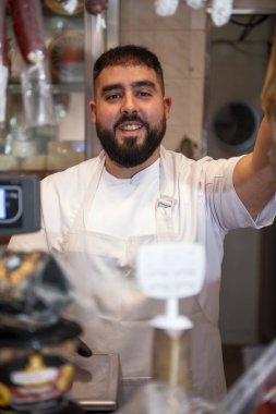 Gülümseyen kasap lezzetli bir Serrano jambonu arıyor, müşterilere ustalıkla hizmet ediyor ve canlı bir kasap dükkanında tezahürat yapıyor