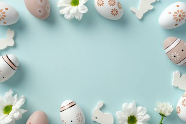 Paskalya çerçevesi. Çiçeksel desenli düz kompozisyon. Paskalya yumurtaları, beyaz papatyalar ve pastel mavi arka planda tavşan kesimleri.