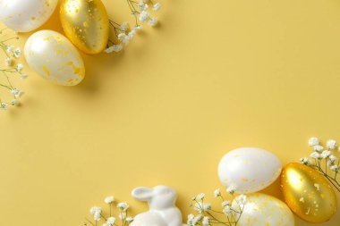 Mutlu Paskalyalar. Düz kompozisyonda altın benekli yumurtalar, beyaz seramik tavşancık ve parlak sarı arka planda narin çiçekler vardı.