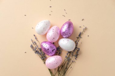 Pastel benekli yumurta, lavanta filizi ve bej arkaplanlı beyaz seramik tavşanlı Paskalya kompozisyonu. Düz yatış, üst görünüm.