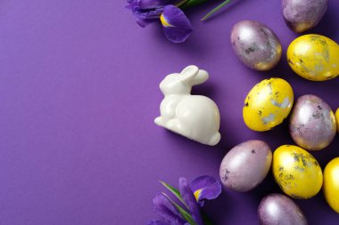 Zarif Paskalya kompozisyonu. Seramik tavşan, mor ve sarı yumurta ve mor arka planda taze irisler.