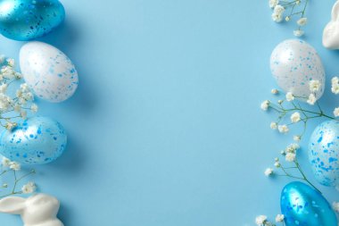 Mavi ve beyaz benekli Paskalya yumurtaları narin çiçekler ve pastel mavi arka planda seramik tavşancık.