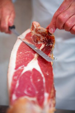 Kasap Serrano jambonunu bıçakla doğruyor, kasap dükkanında müşterilere hazırlıyor.