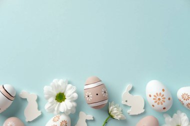 Mavi arka planda süslü Paskalya yumurtaları, papatyalar ve tavşan siluetleri. Düz yatış, üst görünüm