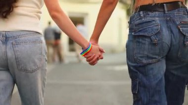 İki kadın el ele yürüyorlar, gökkuşağı bileziklerini ve çantalarını gösteriyorlar, aşklarını ve gururlarını kutluyorlar.