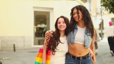 Kadın çift birlikte yürüyor, kucaklaşıyorlar ve gururla gökkuşağı bayrağı sergiliyorlar. Kentin sokak ortamındaki gurur verici kutlamaları sırasında sevinç anlarını paylaşıyorlar.