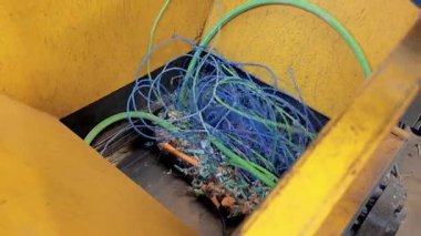 Karışık elektrik kablolarını işleyen bir geri dönüşüm makinesini kapat. Canlı mavi ve yeşil kablolar sürdürülebilir atık yönetimi uygulamalarını vurgulayarak yeniden amaçlanmaya hazırlar.