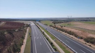 Etrafı tarlalar ve tepelerle çevrili sakin bir kırsal alanda uzanan boş bir otoyolun havadan görünüşü. Açık mavi gökyüzü kırsal kesimin sükunetini arttırır..