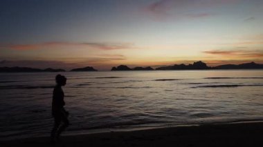 Silüet içinde bir gezgin alacakaranlıkta sakin bir Filipin plajı boyunca gezer, büyüleyici bir günbatımı tarafından çerçevelenir. Huzurlu deniz ve görkemli dağlar mükemmel bir manzara..