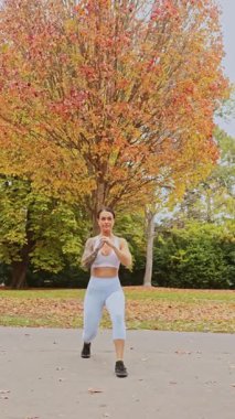 Yeni Zelanda 'da bir sonbahar parkında egzersiz yapan bir kadın. Etrafı canlı sonbahar yapraklarıyla çevrili. Spor kıyafetleri giyip, doğa güzelliğinin ortasında spor ve açık hava aktivitelerini temsil ediyor..