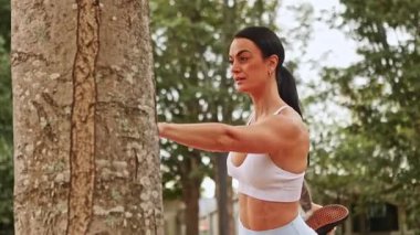 Bir kadın, Yeni Zelanda 'da bir sonbahar parkında bir ağacın kenarına uzanır ve canlı havanın tadını çıkarırken aktif kalır. Sahne, sonbaharın canlı renklerini yakalıyor, sağlığını vurguluyor..