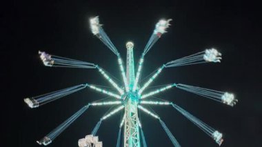 Hareketli bir karnaval gecesi gökyüzüne doğru parlak bir ışık saçan canlı bir kule salıncak. Yolculuk zarifçe dönerken insanlar heyecan verici hava deneyimini seviyorlar.