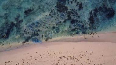 Yumuşak dalgaların kıyıya vurduğu sakin bir sahilin büyüleyici hava manzarası. Sahil güzelliği ve rahatlığı gösteren seyahat ve turizm görselleri için ideal.